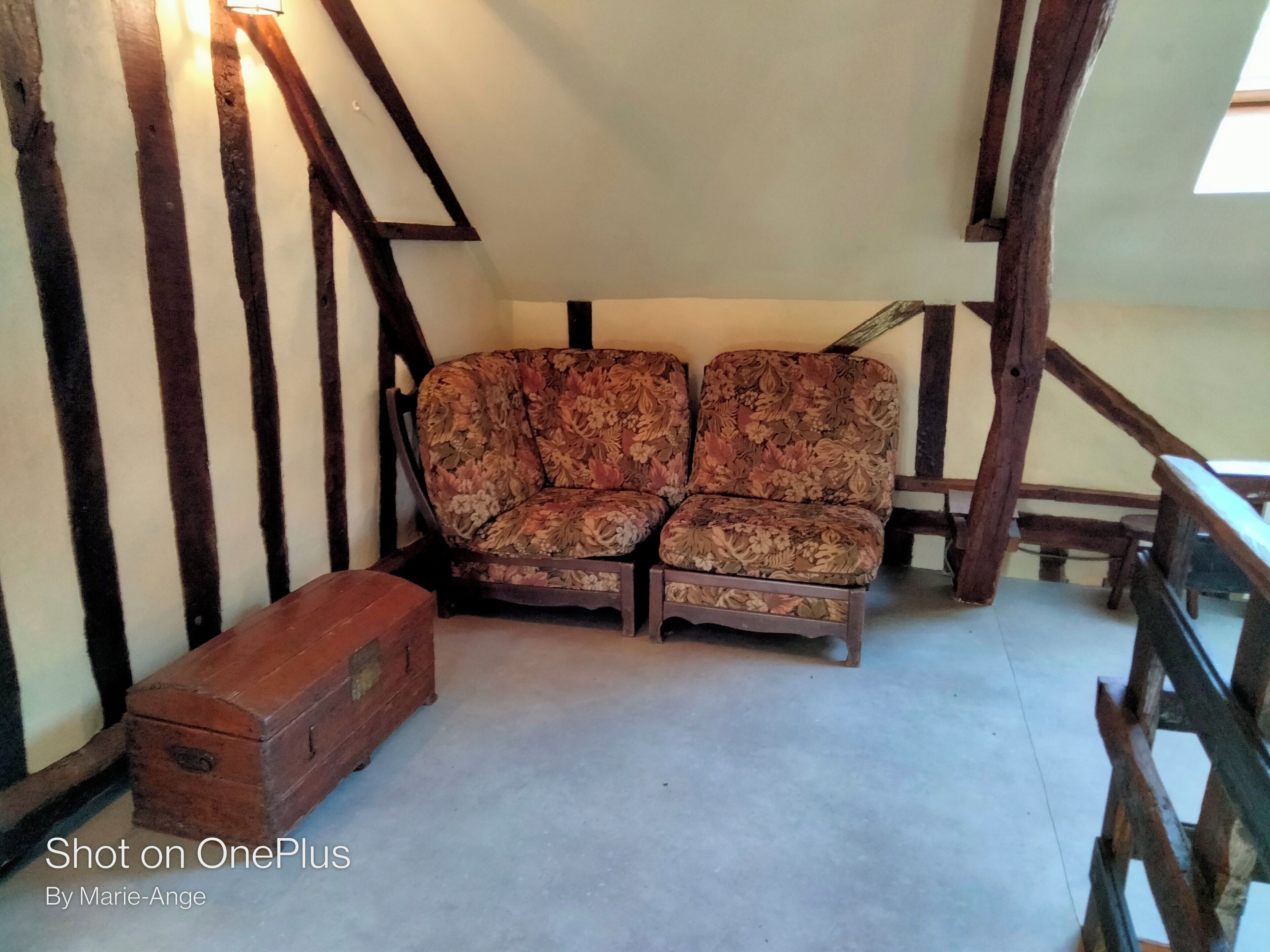 Une pièce avec un canapé à motifs floraux, une commode en bois et des poutres apparentes.