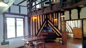 Ein Zimmer mit freiliegenden Holzbalken, einem Esstisch mit Stühlen, einem Fernseher auf einer Holzkommode und einer Treppe, die zu einer oberen Ebene führt.