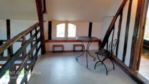 Ein Zimmer mit schrägem Dach, einem kleinen Tisch mit Stuhl, einem Fenster mit Blick und einer Holztreppe.