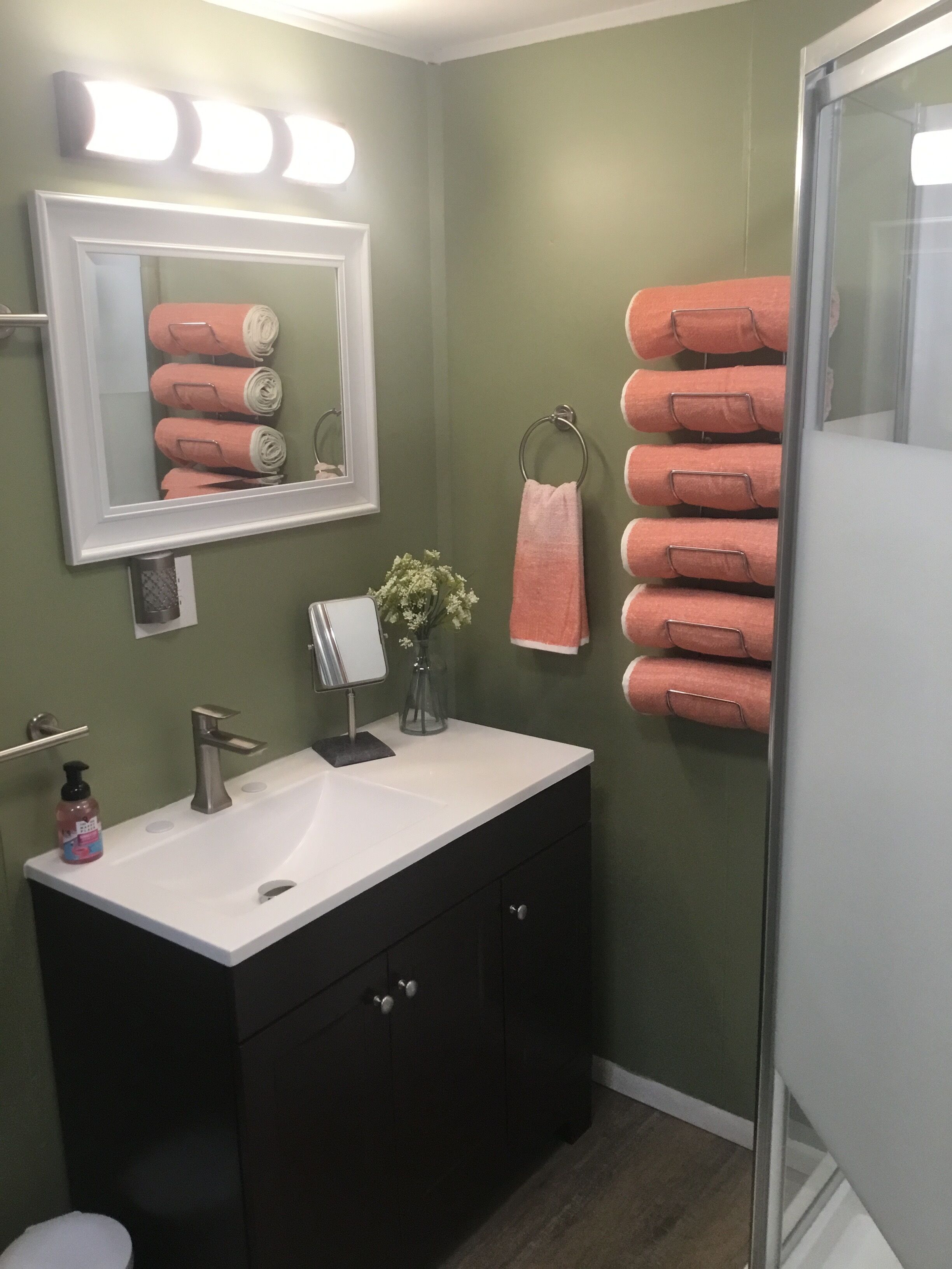 Un baño con un lavabo blanco, armarios oscuros, un espejo con luces y varias toallas rosas.