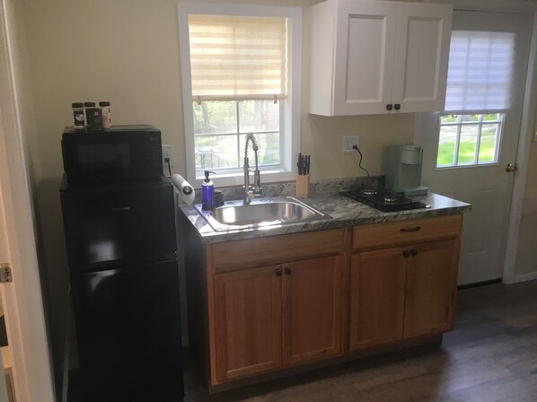 A kitchen with a black refrigerator, a sink, wooden cabinets, and a window with blinds.