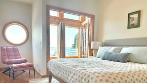 Un dormitorio con una cama grande, una silla, un espejo redondo y vistas al exterior.