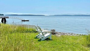 Escena junto al lago con un muelle, una silla blanca y un tocón de madera.