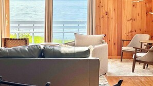 Una habitación con interior de madera, un ventanal con cortinas, un sofá, una silla y una mesita.