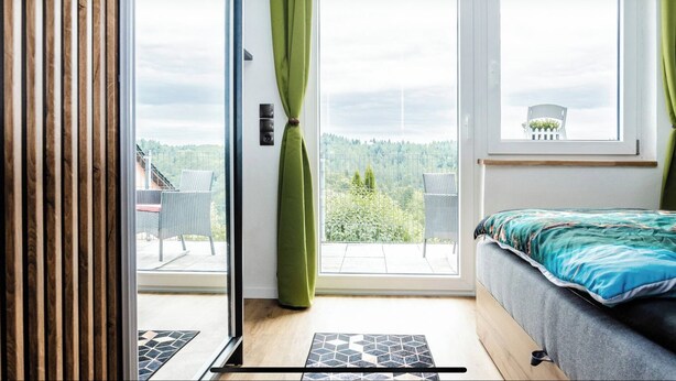 A bedroom with a bed, a sliding glass door leading to a balcony, and a view of a forested area. - New and fully equipped Wonderful view (Saldenburg)