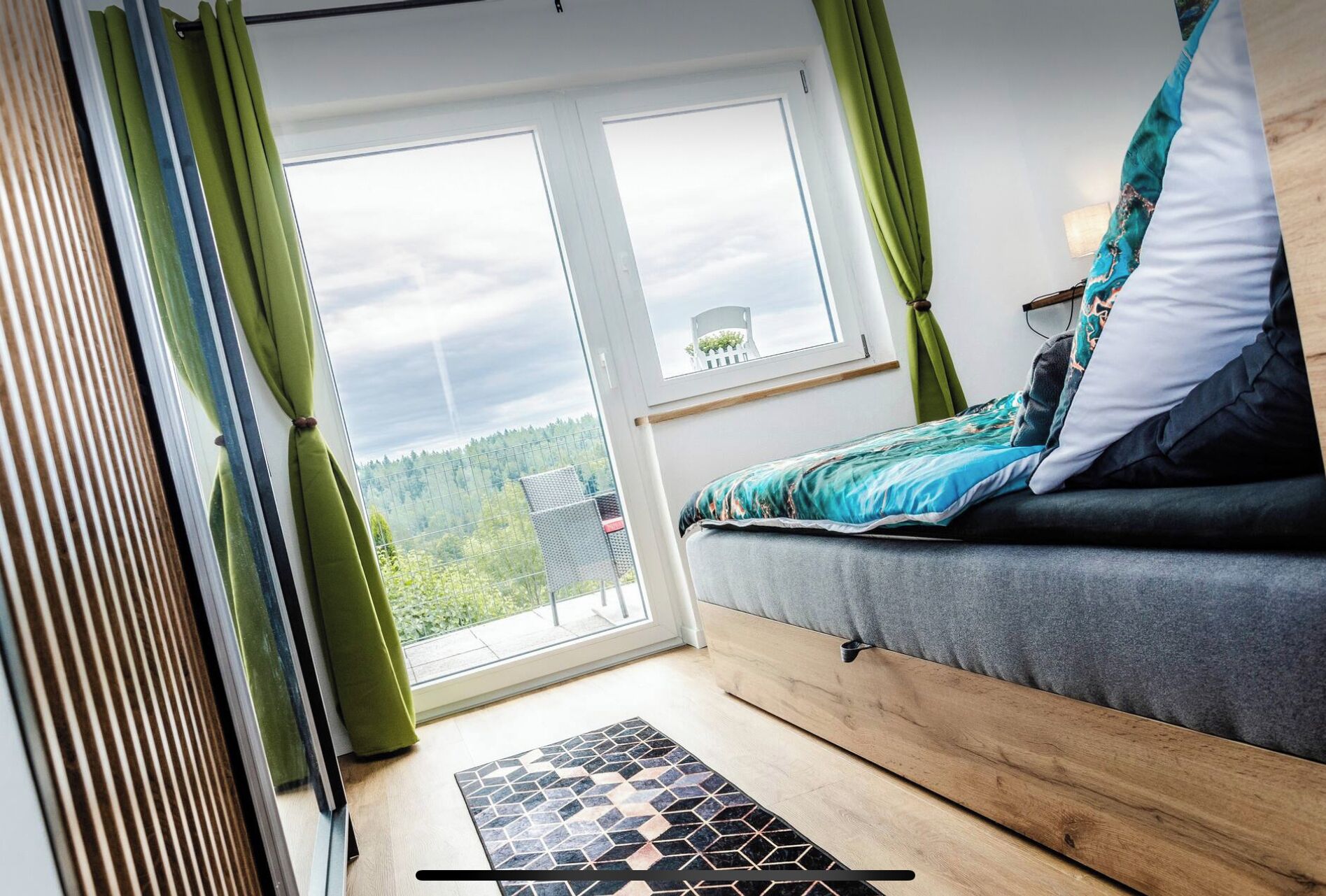 Ein modernes Schlafzimmer mit einem Bett, einem Fenster mit Blick auf einen Wald und einer Tür mit Vorhängen.