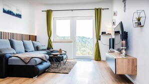 A modern living room with a sofa, a coffee table, a TV, and a wooden sideboard. - New and fully equipped Wonderful view (Saldenburg)