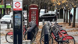 A row of bicycles parked on a sidewalk, a red telephone booth, and a map information kiosk.