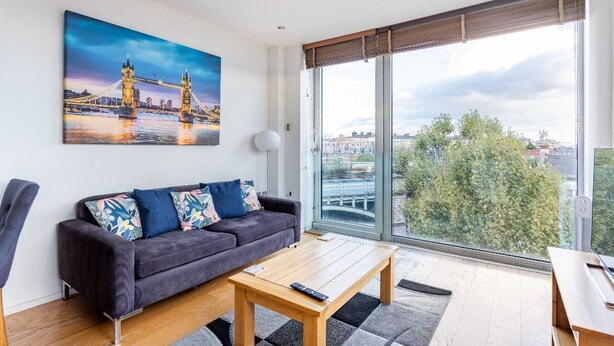 A modern living room with a large window, a sofa, a coffee table, and a painting of a bridge.