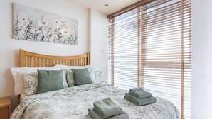 A bedroom with a wooden headboard, a floral bedspread, and a large window with blinds.