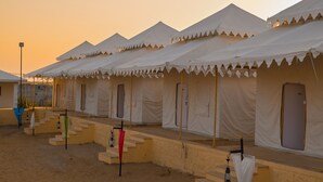 A row of white tents with a flat roof, arranged in a linear fashion with a sandy ground and a few steps leading up to the entrance. - Shrinath Desert Camp (Jaisalmer)