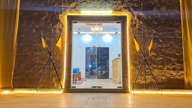 An entrance with a stone wall, a chandelier, and a view of the outside. - Shrinath Desert Camp (Jaisalmer)