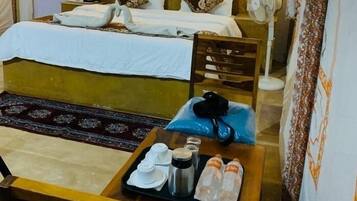 Una habitación de hotel con una cama, una silla de madera, una mesita con artículos de aseo y un ventilador.