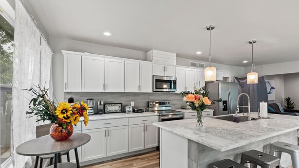 Une cuisine moderne avec des meubles blancs, un îlot central, des appareils en acier inoxydable et des luminaires suspendus.