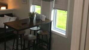 Ein Essbereich mit Holztisch und Barhocker, einem flachbildfernseher über einem Fenster sowie Blick ins Freie.