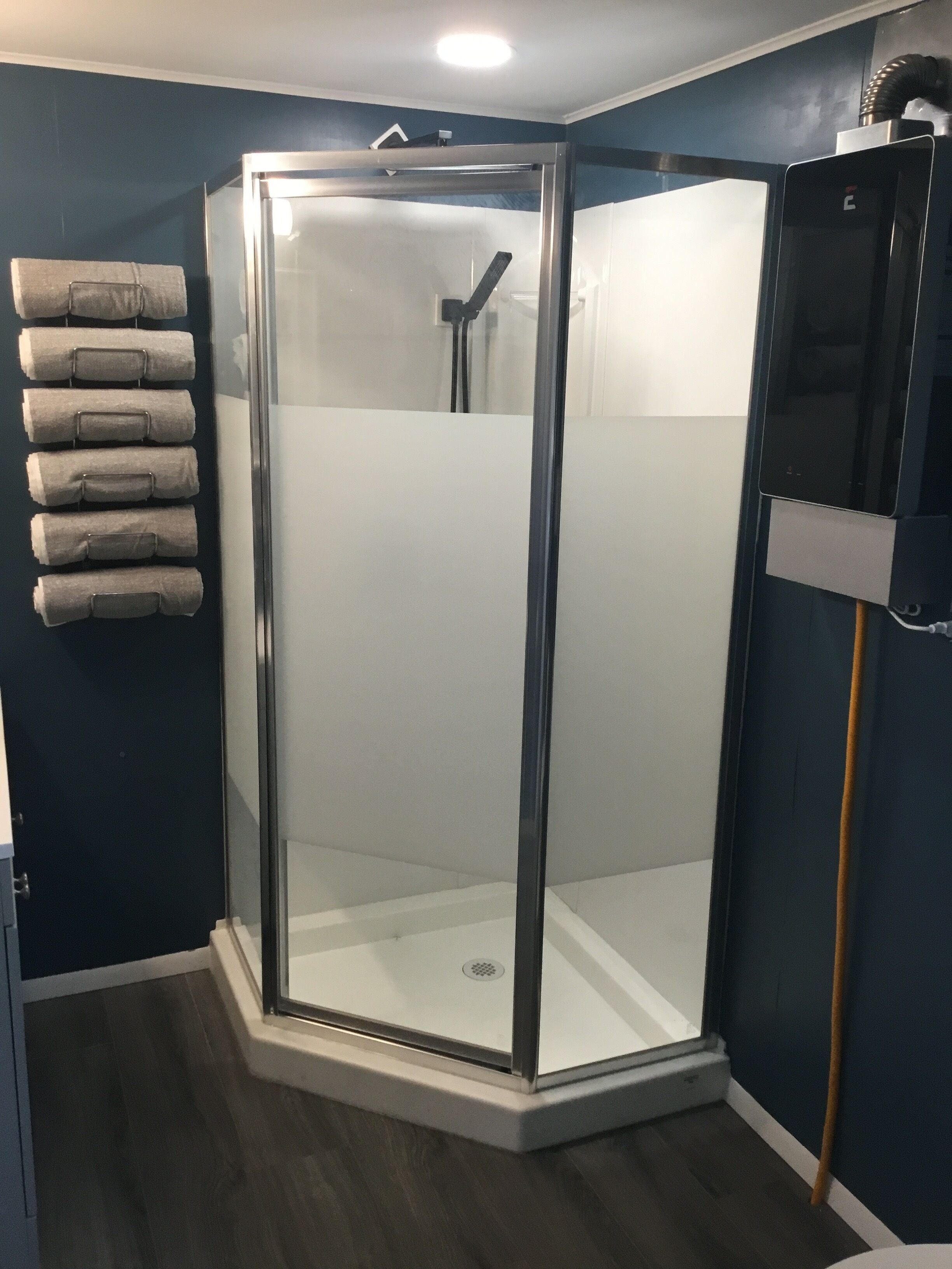 A glass-enclosed shower with a white floor, dark walls, and a towel rack with towels.