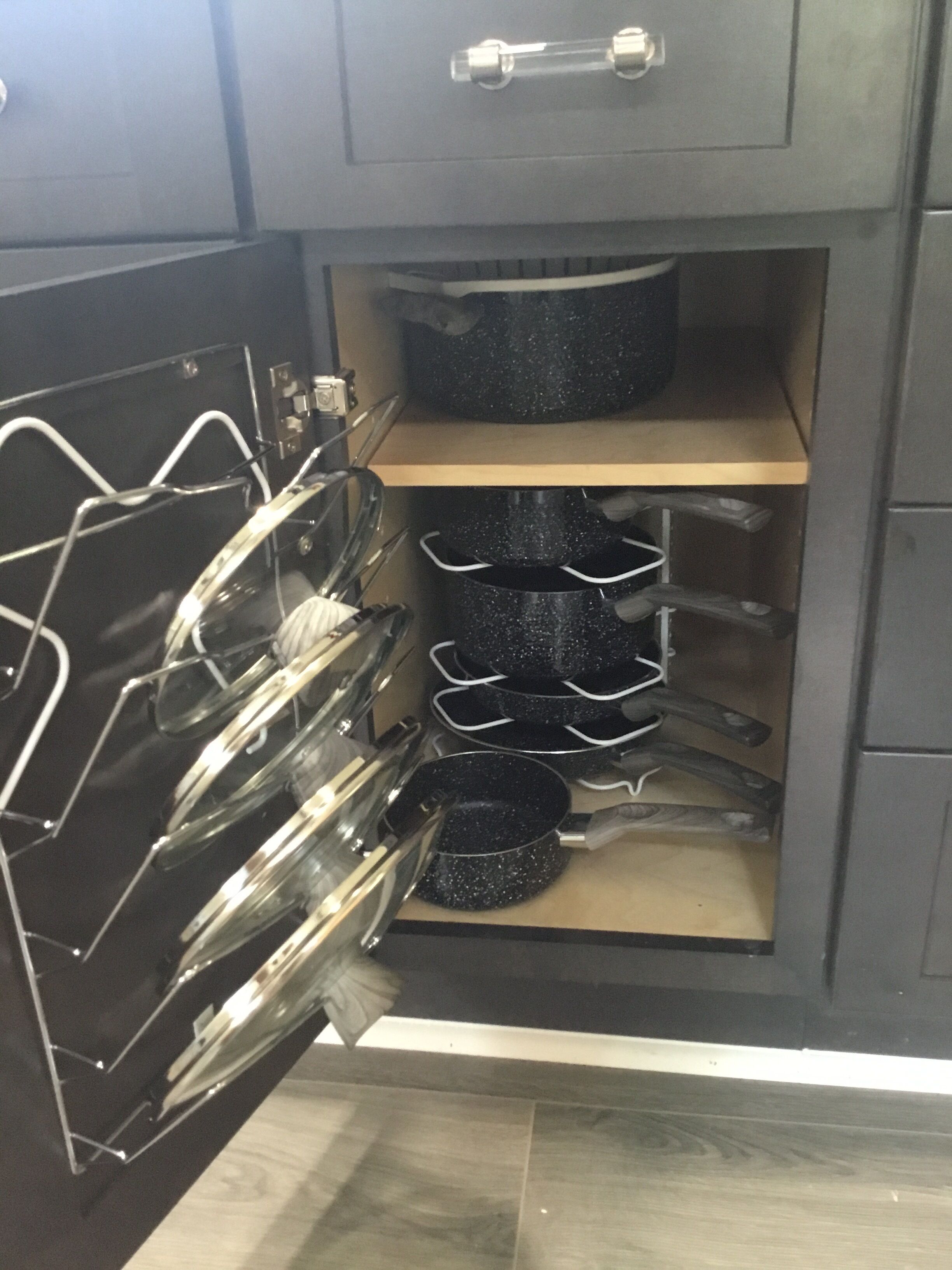An open kitchen cabinet with a utensil rack and multiple black pots and pans stored inside.