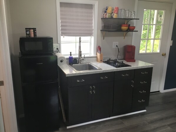A kitchen with a black refrigerator, a sink, a stove, and a window with blinds.