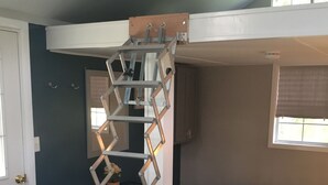 Ein Zimmer mit Etagenbett, einer Leiter, einer Couch mit Zierkissen, einem Fenster und einer Tür.