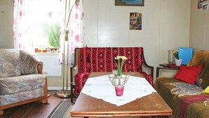 En stue med en sofa med blomstermønster, en rød lænestol med et mønster, et træbord med en blomstervase og en gulvlampe.