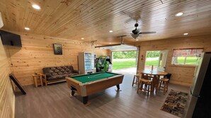 A wooden interior with a pool table, a sofa, a dining table with chairs, and a vending machine. - Bluegill Bungalow-9 Miles To Dells, Pet Friendly (Briggsville)