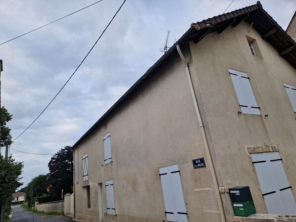 A beige building with white shutters, a sign reading "RUE DE LA VALLEE," and a green utility box.