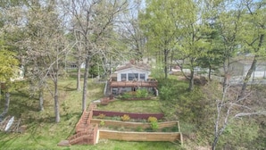 Ein zweistöckiges Haus mit Veranda, umgeben von Wald und einem kleinen Garten mit erhöhten Beeten.