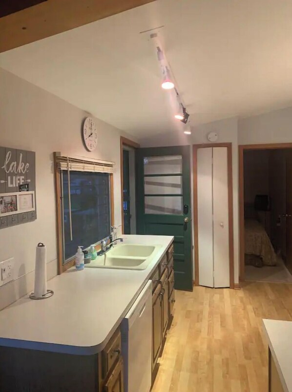 A kitchen with a double sink, a clock, and a door leading to another room. - Lakefront home away from home.
 (Lakeview)