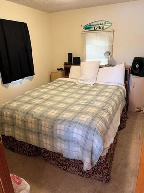 A neatly made bed with a plaid bedspread, a bedside table with a lamp, and a sign above the window that reads "Welcome to the Lake." - Lakefront home away from home.
 (Lakeview)