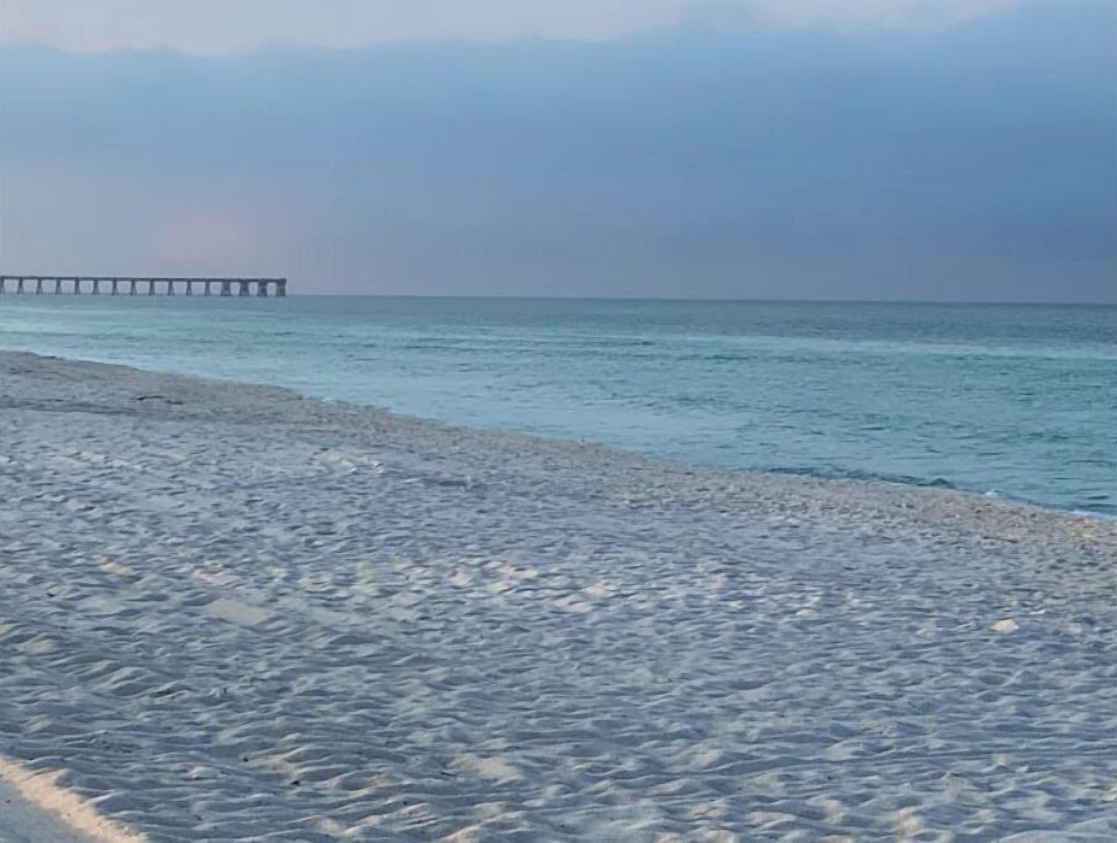 Una playa con un muelle que se adentra en aguas tranquilas.