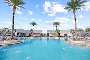 A swimming pool with palm trees and lounge chairs, surrounded by buildings with a modern design.