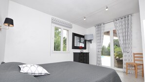Ein Schlafzimmer mit Bett, Kommode, Fernseher und Blick auf ein Freibad.