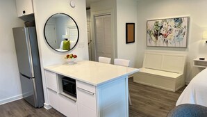 A compact kitchen with a refrigerator, a white countertop, and a mirror. There is a dining area with a white table and chairs. - Newly remodeled, heart of Seagrove Beach, 100 yards to beach! (Santa Rosa Beach)