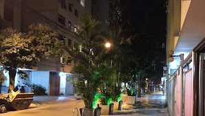 Una calle iluminada de noche con aceras pavimentadas, palmeras y edificios.