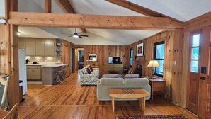 A spacious living area with a wooden ceiling, a fireplace, a television, and a kitchen in the background. - Fern Hill Cabin - near Dupont State Forest (Brevard)