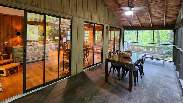 A spacious room with large sliding glass doors leading to an outdoor deck, wooden floors, and a ceiling fan. - Fern Hill Cabin - near Dupont State Forest (Brevard)