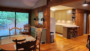 A wooden interior with a dining area, kitchen, and large windows overlooking greenery. - Fern Hill Cabin - near Dupont State Forest (Brevard)