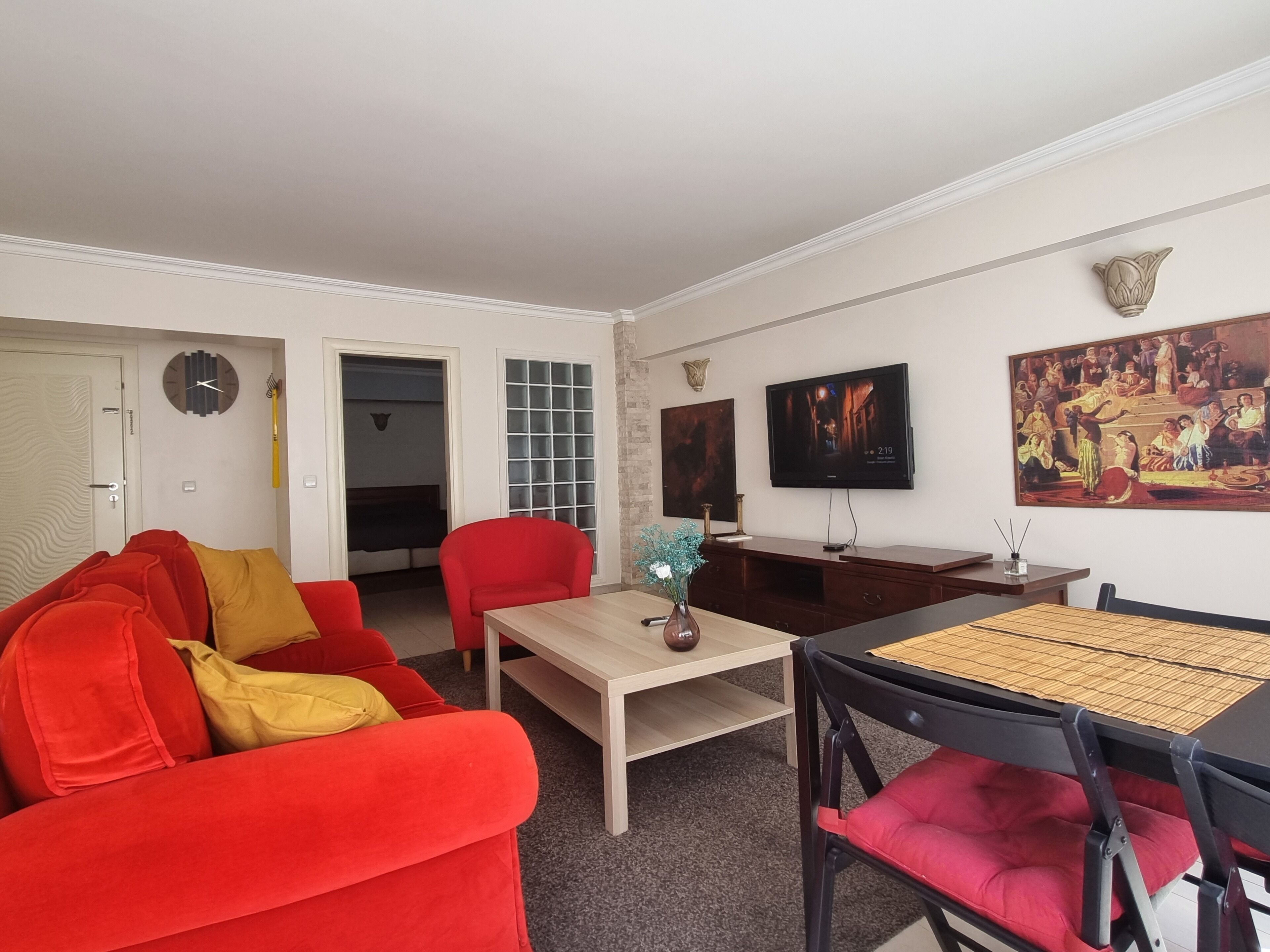 A living room with a red sofa, a wooden coffee table, a TV, and artwork on the walls.