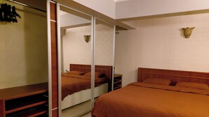 Un dormitorio con un armario espejado, un cabecero de madera y una pared de ladrillo blanco.