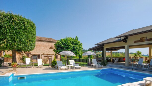 A pool area with lounge chairs and umbrellas, a stone building, and a covered seating area. - Cozy apartment in Monte Rinaldo (Monte Rinaldo)