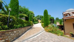 A paved pathway leading through a garden with tall, narrow trees and a stone wall on one side. - Cozy apartment in Monte Rinaldo (Monte Rinaldo)