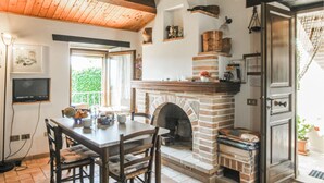 A rustic kitchen with a brick fireplace, wooden ceiling, and a dining area with a table and chairs. - Cozy apartment in Monte Rinaldo (Monte Rinaldo)