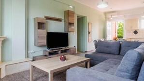 A living room with a flat-screen TV, grey sofa, wooden coffee table, and a dining area with a table and chairs.