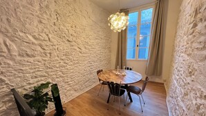 A dining area with a round wooden table, four chairs, a hanging light fixture, and a window with curtains. - Maisonnette Centre Historique de Nîmes Tout Équipé ! (Nîmes)