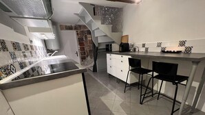 A modern kitchen with a central island, a built-in stove, and a small bar area with stools. - Maisonnette Centre Historique de Nîmes Tout Équipé ! (Nîmes)