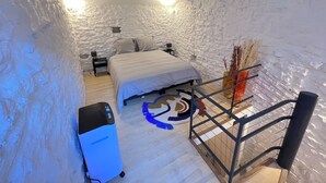A bedroom with a bed, a nightstand, a desk, a chair, a radiator, and a decorative plant. - Maisonnette Centre Historique de Nîmes Tout Équipé ! (Nîmes)