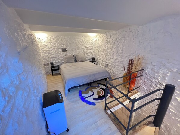 A bedroom with a bed, a nightstand, a desk, a chair, a radiator, and a decorative plant. - Maisonnette Centre Historique de Nîmes Tout Équipé ! (Nîmes)