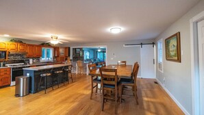 Una cocina amplia con armarios de madera, una isla central con taburetes de bar y un comedor con mesa y sillas de madera.