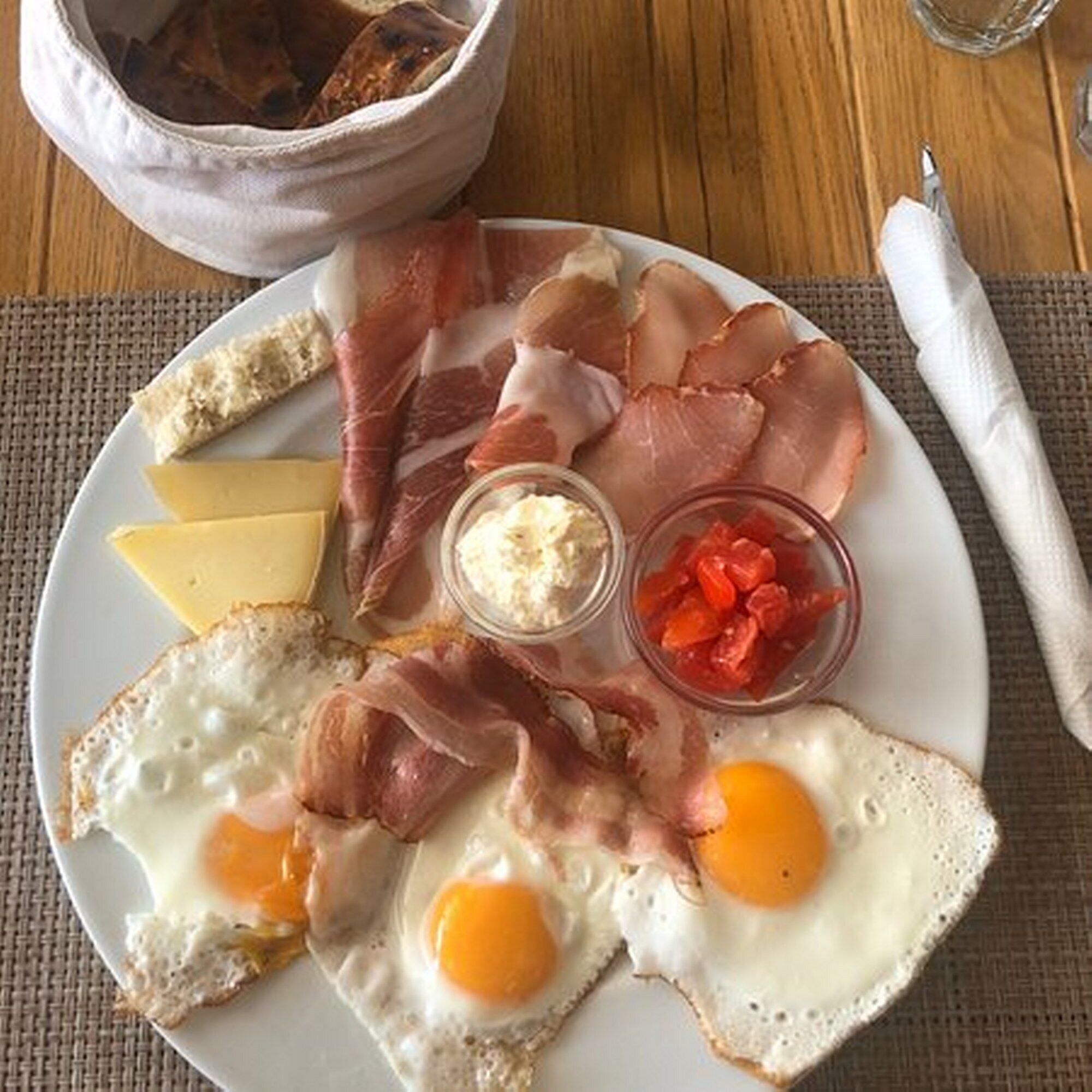 A plate with eggs, bacon, cheese, and a small bowl of tomatoes.