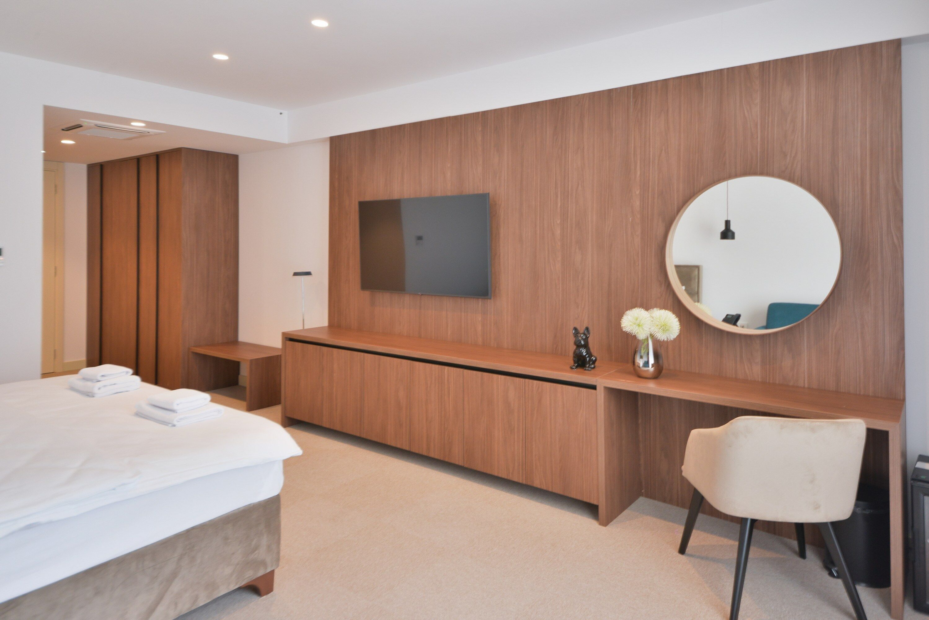 Ein modernes Hotelzimmer mit einem Bett, einem Holzinlay und einem runden Spiegel sowie einem Sessel.